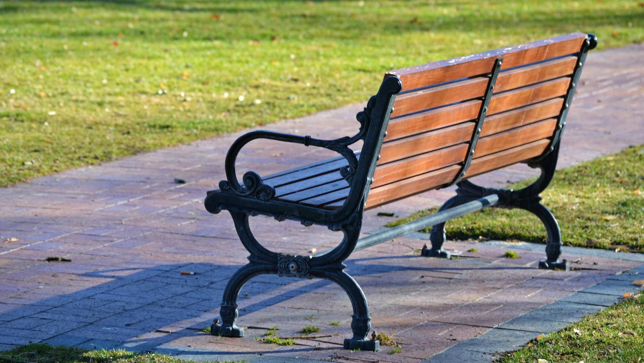 A picturesque vintage wooden bench in a sunny park with a paved pathway.