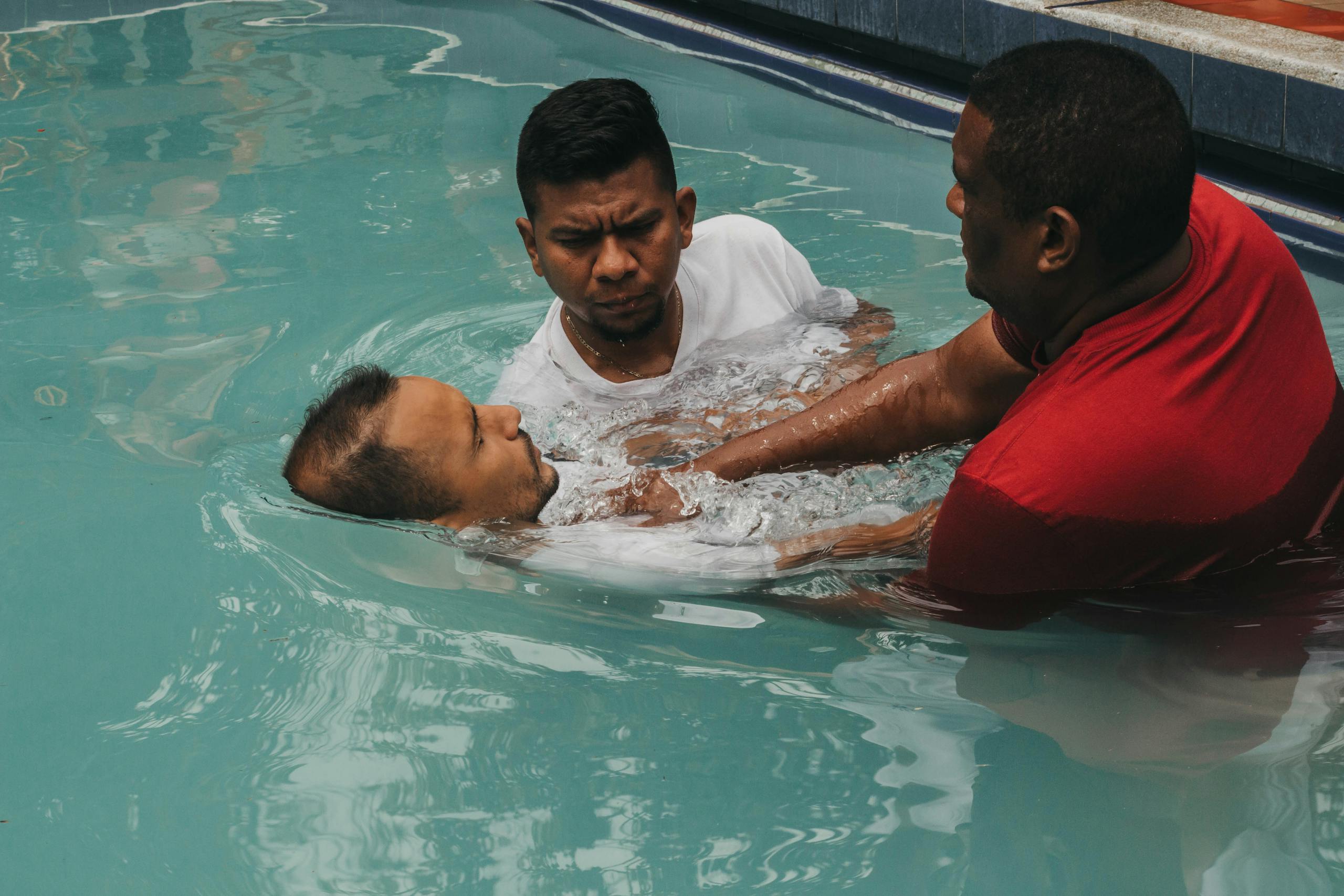 Three men performing a baptism in a swimming pool, symbolizing faith and tradition.