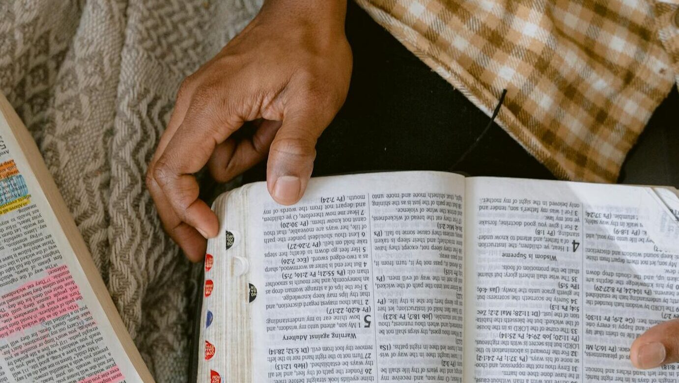 Two adults reading religious texts with highlighted passages indoors, sharing a moment of learning and connection.